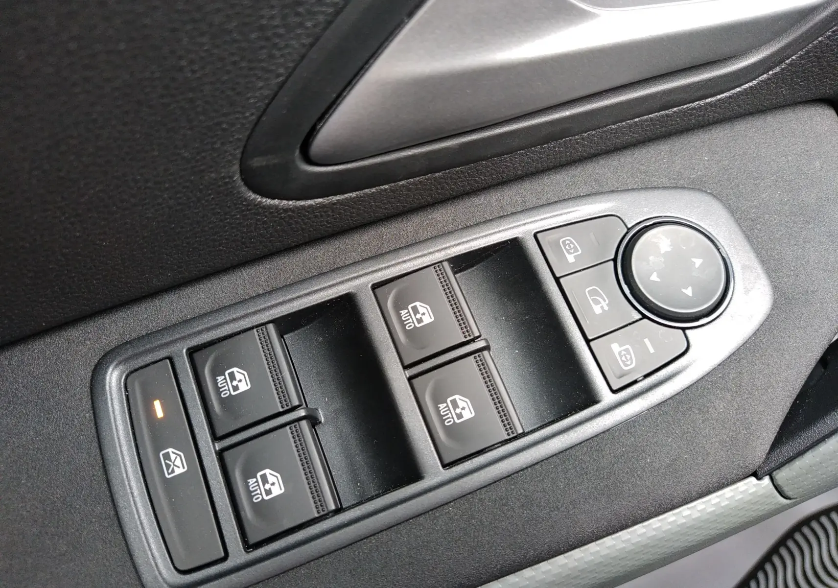 Gros plan sur les commandes des vitres électriques et rétroviseurs côté conducteur du Dacia Duster Hybrid-G couleur Sandstone.
