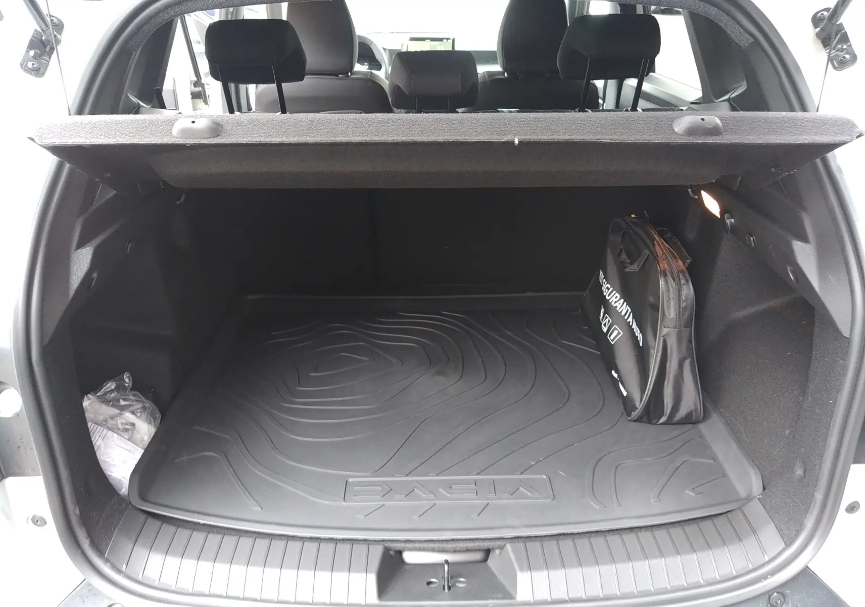 Vue arrière ouverte du coffre du Dacia Duster 2026, avec tapis de sol noir et sac de rangement visible.
