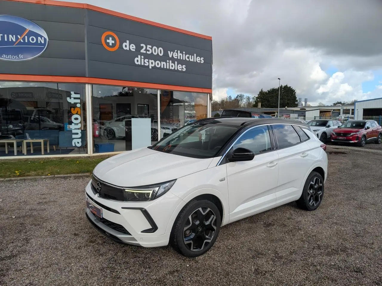 Opel Grandland blanc métallisé en 3/4 avant droit avec toit noir et jantes alliage noires sur parking.