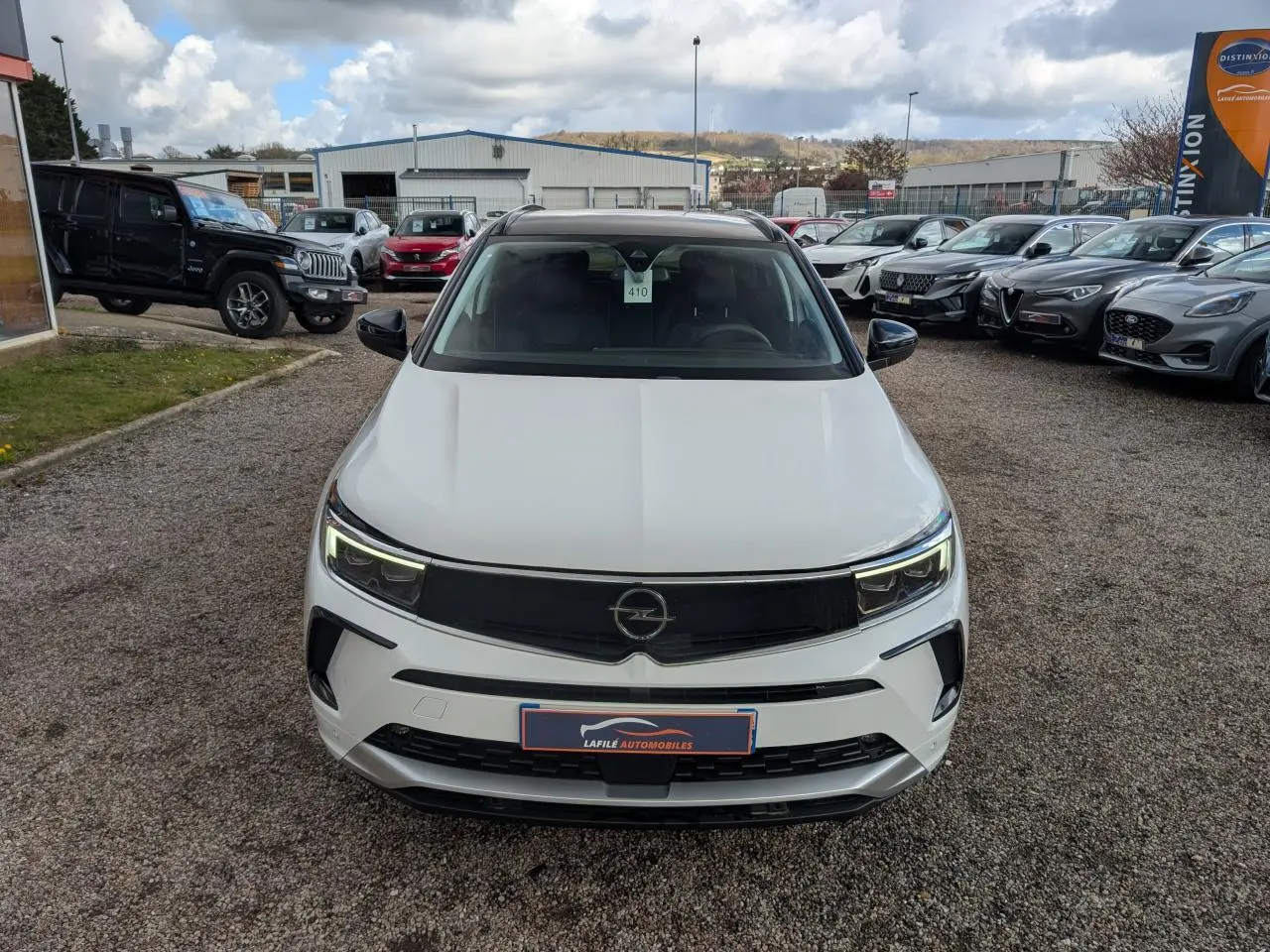 Vue avant d'un Opel Grandland blanc métallisé avec calandre noire et phares LED allumés sur un parking extérieur.