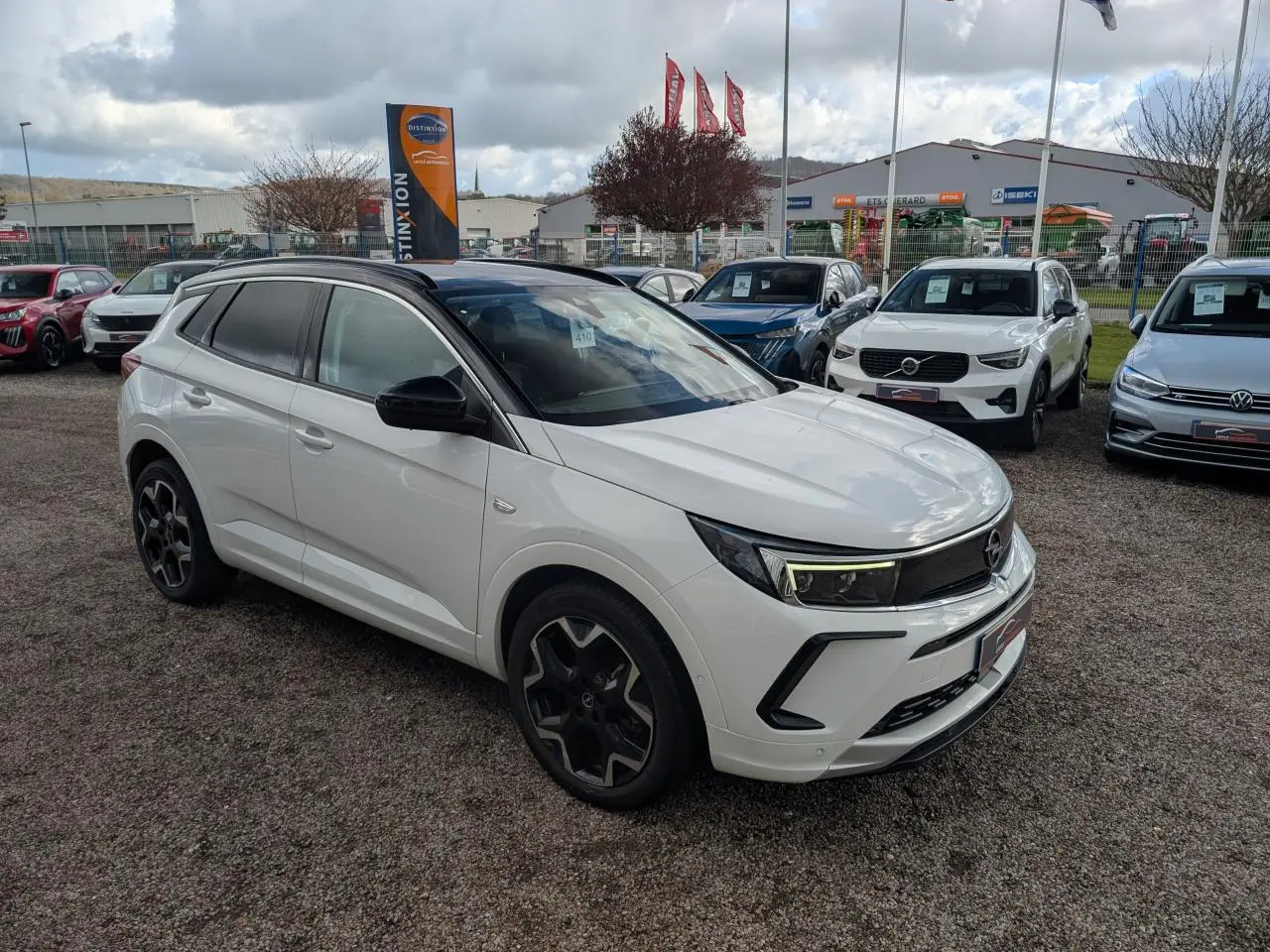 Opel Grandland blanc métallisé en 3/4 avant droit avec toit noir et jantes alliage noires sur parking.
