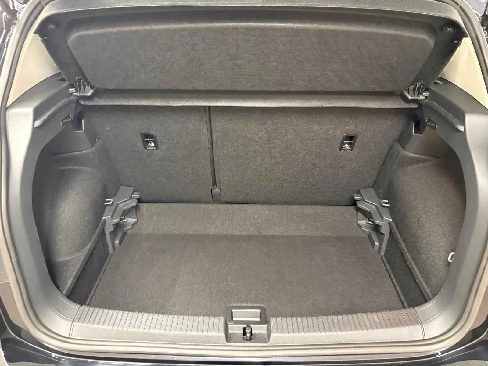 Coffre ouvert du Volkswagen T-Cross noir intense 2024, vue arrière montrant l'espace de chargement vide et la tablette cache-bagages relevée.