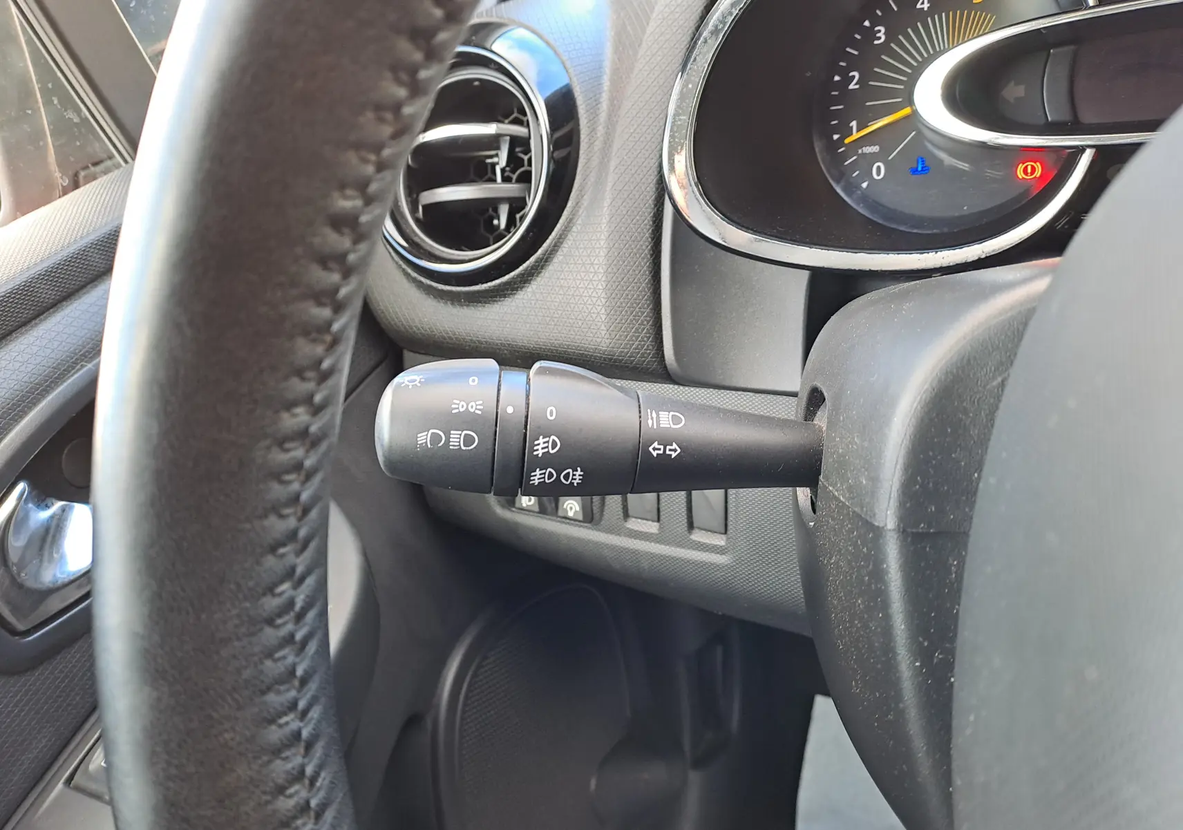 Gros plan sur la manette de commande des phares et clignotants à gauche du volant dans l'habitacle noir d'une Renault Clio IV rouge.