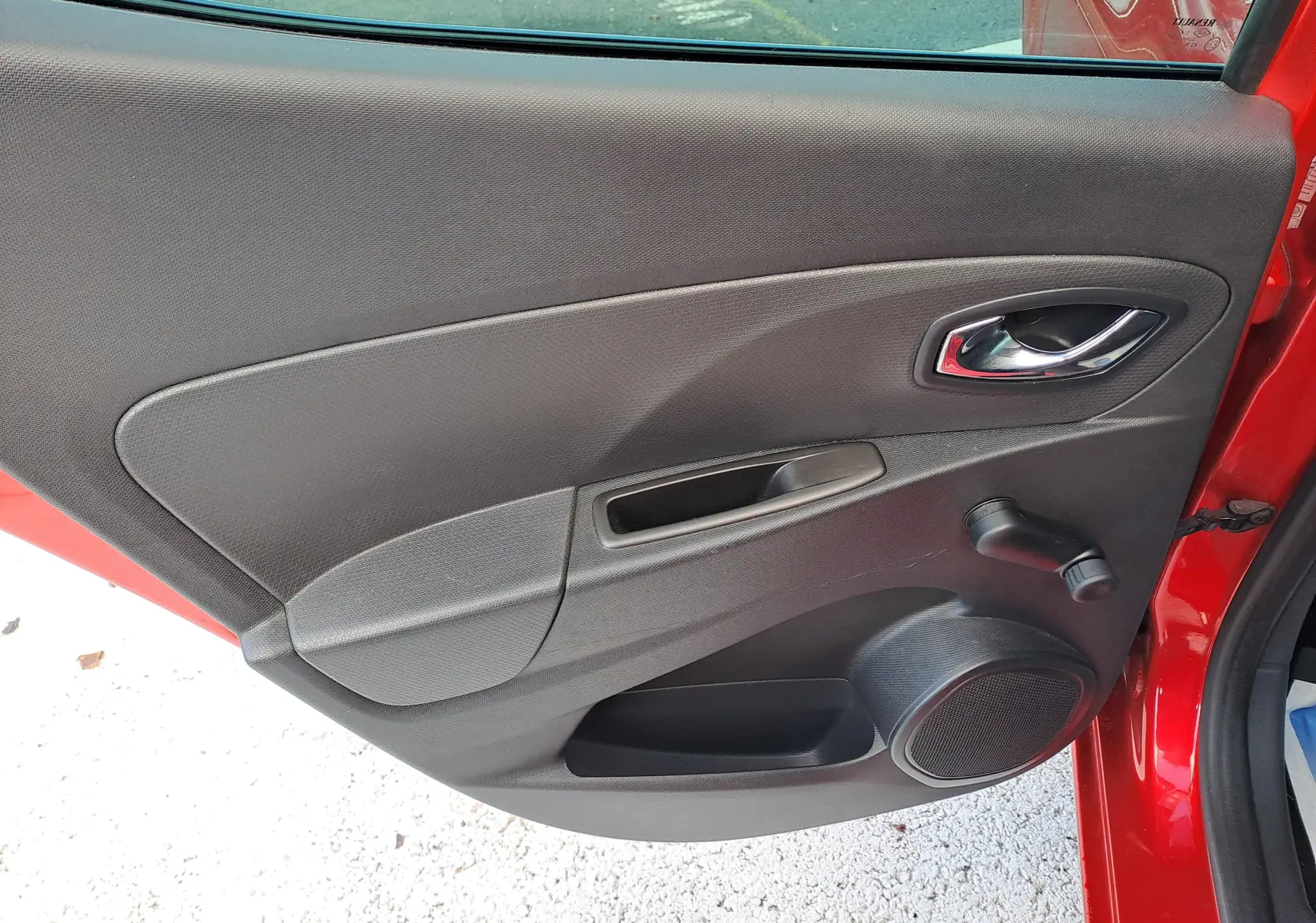 Vue intérieure de la porte arrière gauche rouge d'une Renault Clio IV 1.5 DCI 75 Limited avec commande manuelle de vitre.