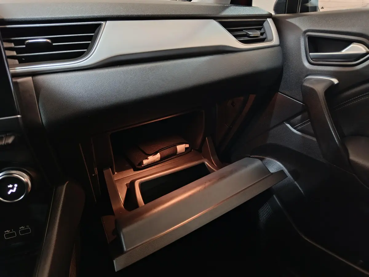 Intérieur noir du Renault Captur 2024, vue côté passager avec boîte à gants ouverte et éclairage intérieur doux.