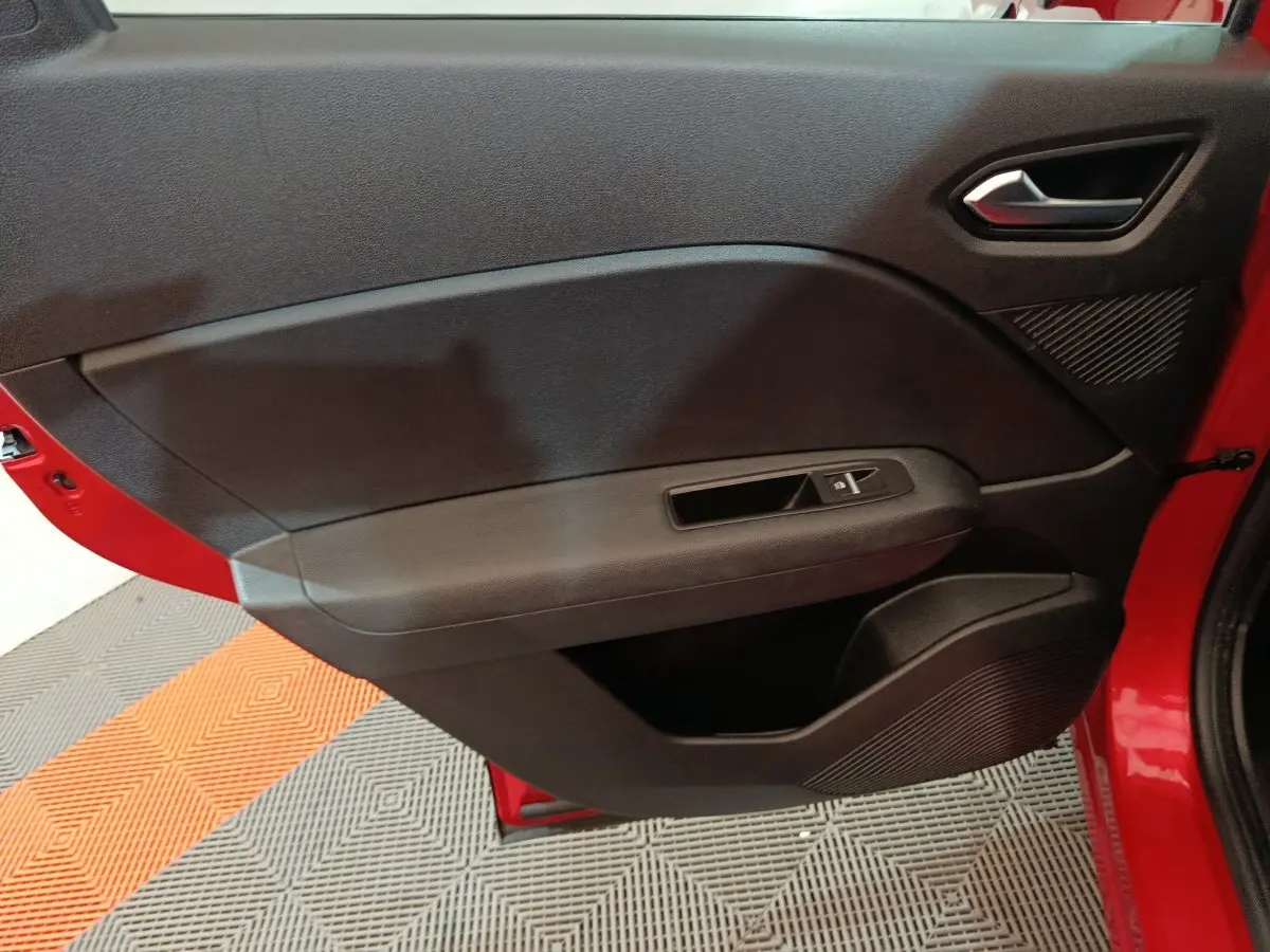 Vue intérieure côté gauche de la porte avant rouge du Renault Captur 2024 avec panneau de commande des vitres noir.