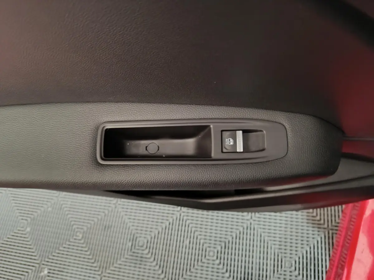 Gros plan sur la commande de lève-vitre côté conducteur d’une Renault Captur rouge, intérieur noir.