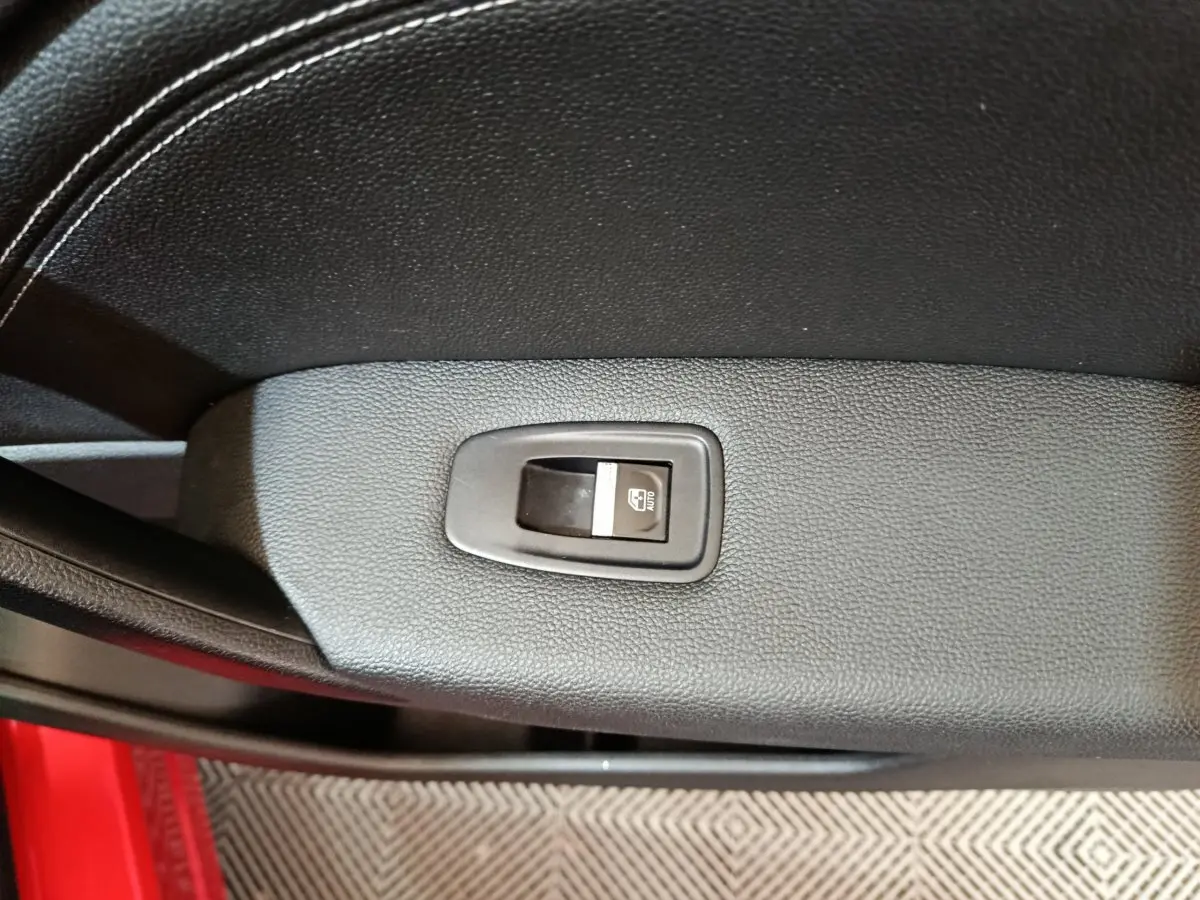 Détail de la commande de lève-vitre sur la porte intérieure noire du Renault Captur rouge 2024, côté conducteur.