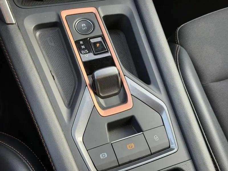 Gros plan sur la console centrale de la SEAT LEON 2025 avec levier de boîte auto entouré d’un cadre cuivre et sièges en cuir noir.