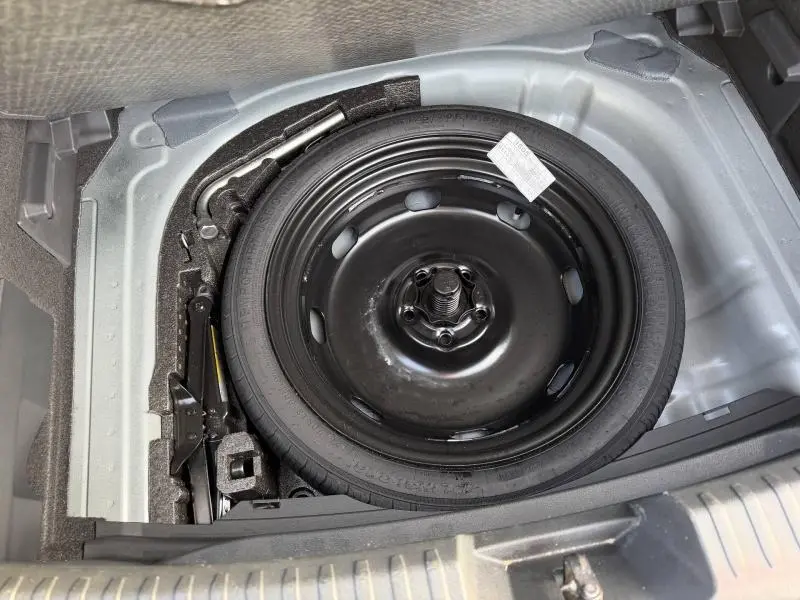 Vue en plongée sur la roue de secours noire dans le coffre d’une SEAT LEON 1.5 eTSI Hybrid 2025, sans visibilité extérieure.
