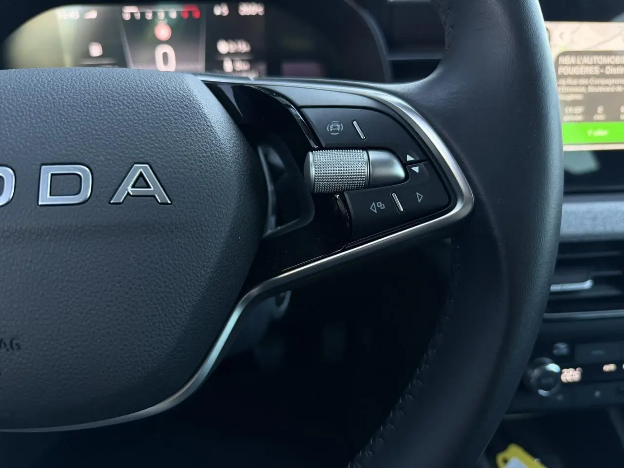 Gros plan sur le volant cuir noir multifonctions de la Skoda Scala TSI 116, avec commandes intégrées et tableau de bord numérique flou en arrière-plan.
