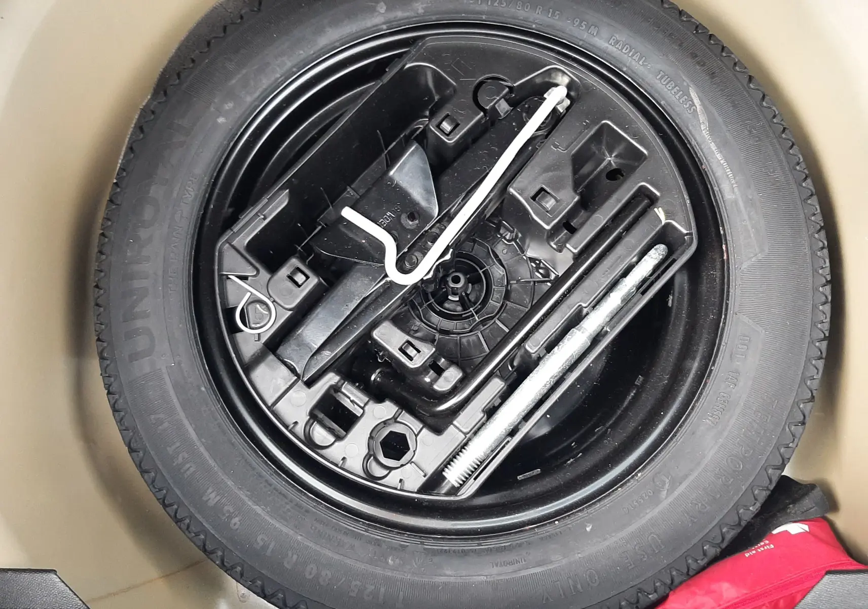 Gros plan sur la roue de secours et les outils de bord dans le coffre d'une Peugeot 208 gris Artense 2025.