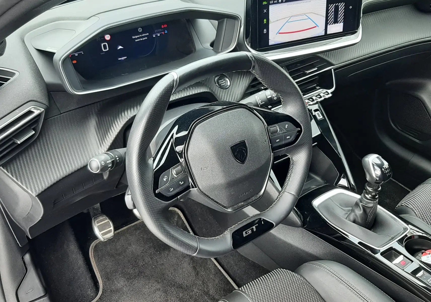 Vue intérieure côté conducteur de la Peugeot 208 GT 1.2 essence 2025, volant GT, écran tactile avec caméra de recul et boîte manuelle.