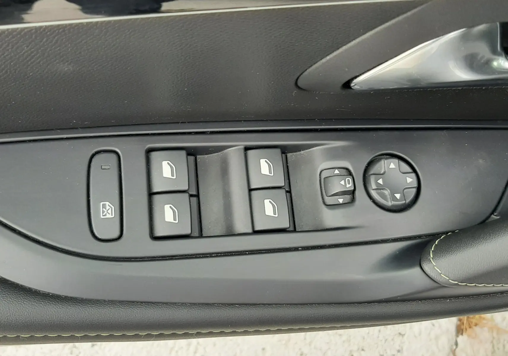 Gros plan sur les commandes des vitres et rétroviseurs côté conducteur d'une Peugeot 208 gris Artense, avec surpiqûres vertes.