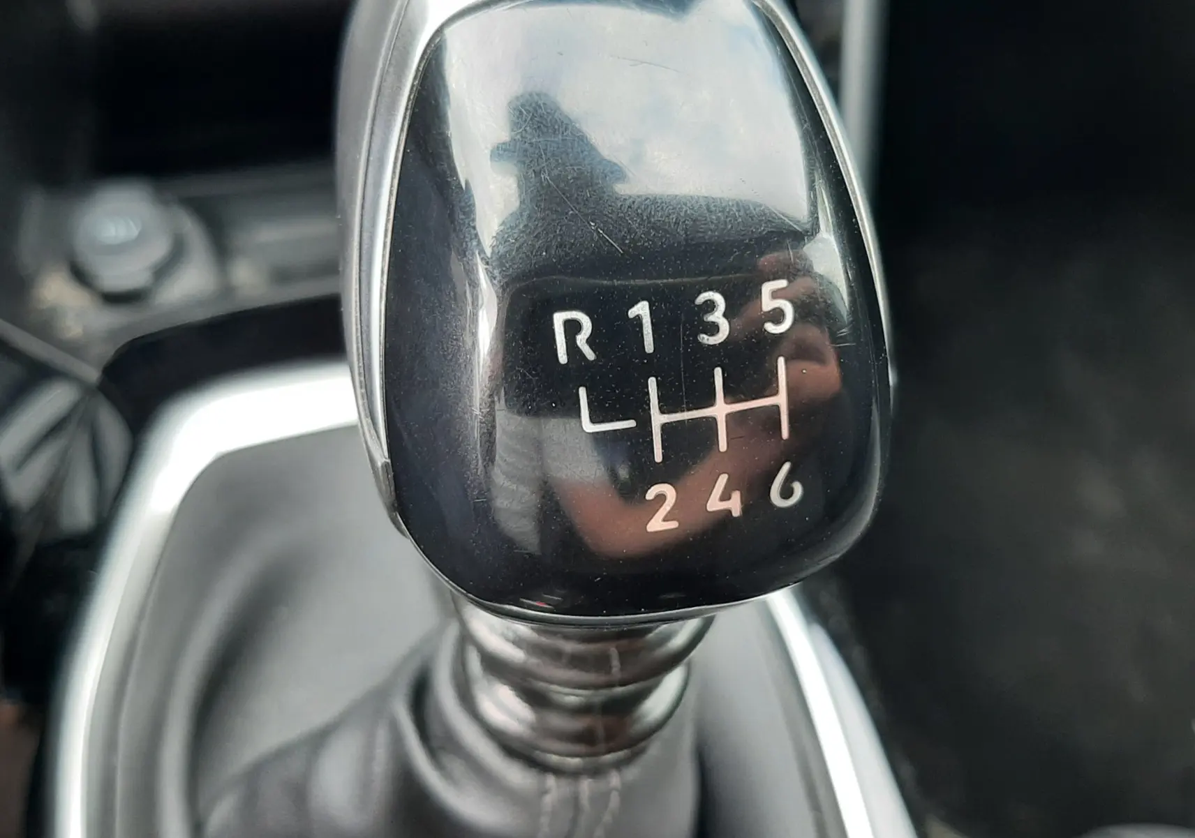 Gros plan sur le levier de vitesses manuel noir brillant de la Peugeot 208 1.2 100CH S&S GT, intérieur gris.