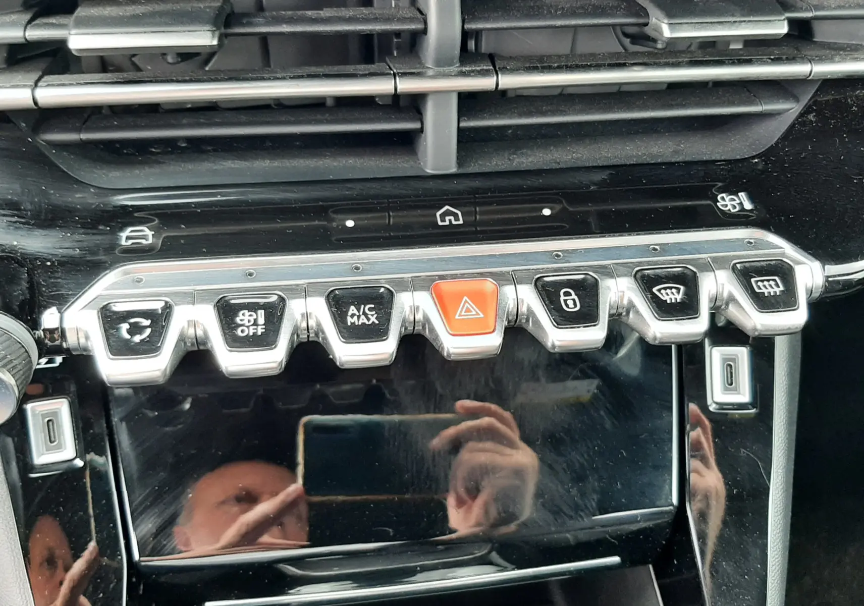 Gros plan sur la console centrale noire brillante de la Peugeot 208 gris Artense, avec boutons chromés et touches de commande.