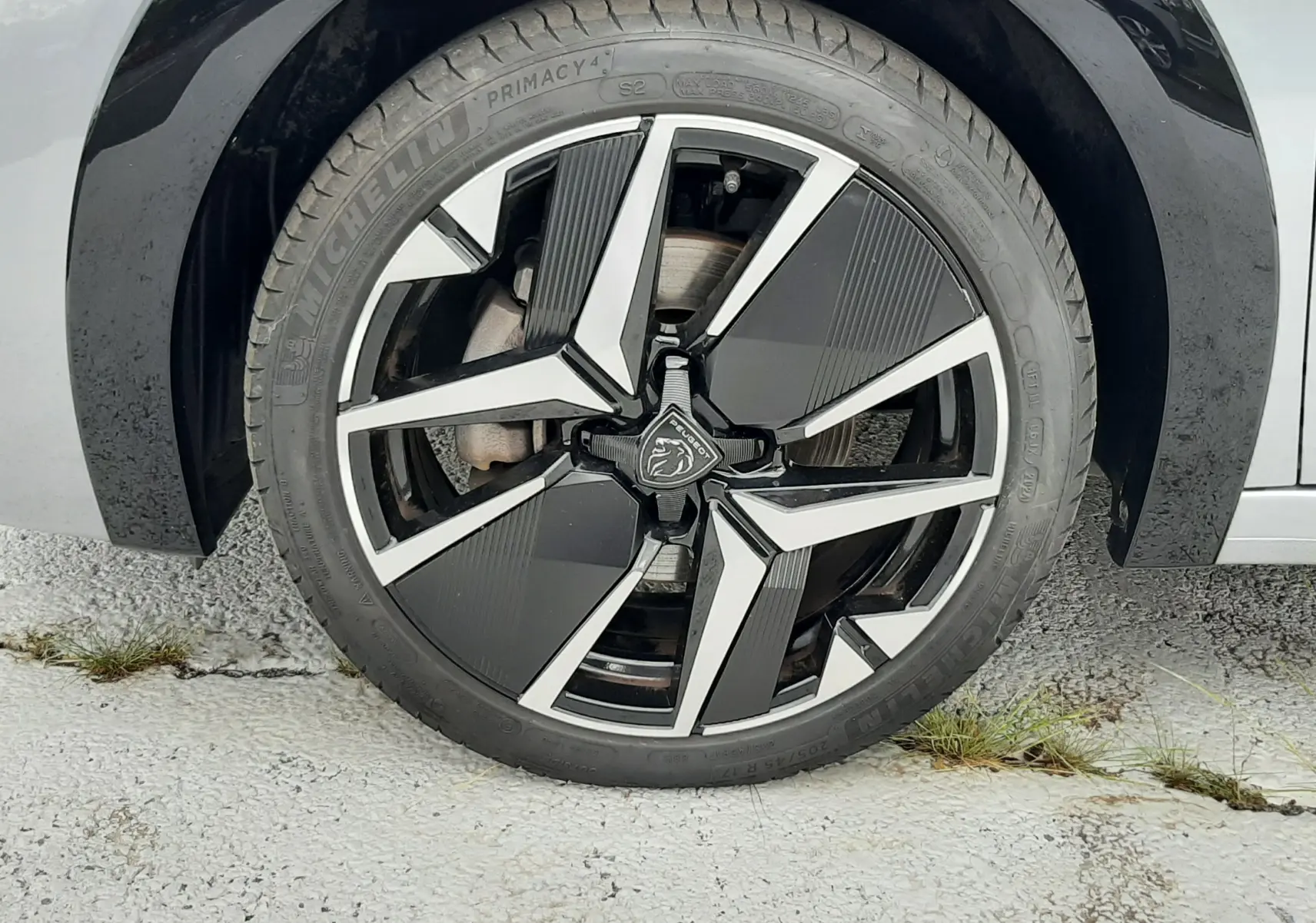 Gros plan sur la roue avant droite de la Peugeot 208 gris Artense, mettant en valeur la jante noire et argentée au design moderne.
