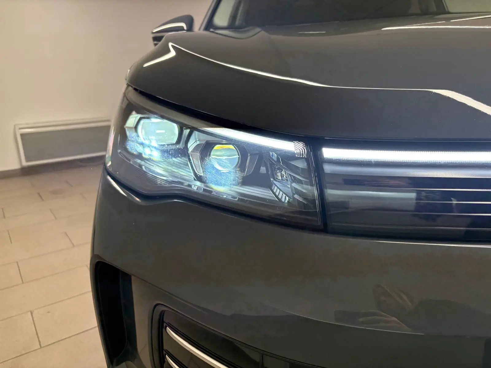 Gros plan sur le phare avant gauche du Volkswagen Tiguan 2025 gris Dauphin avec éclairage LED allumé.
