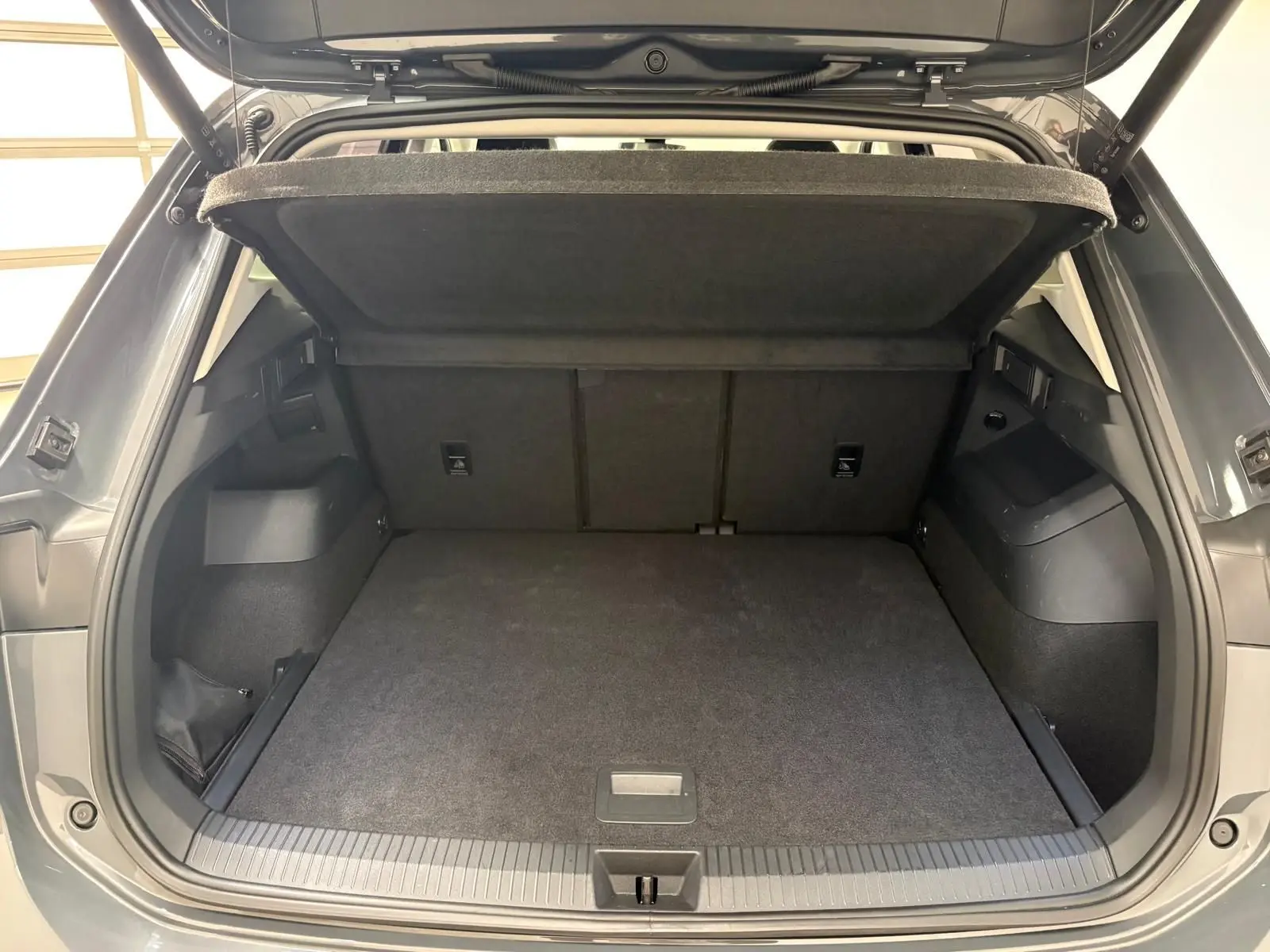 Vue arrière du coffre ouvert du Volkswagen Tiguan 2.0 TDI Gris Dauphin, montrant l'espace de chargement et la tablette cache-bagages.