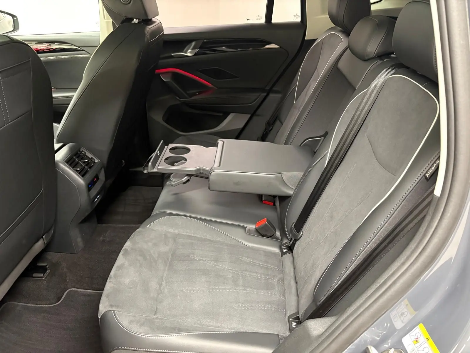 Vue intérieure côté droit des sièges arrière gris clair du Volkswagen Tiguan 2025 avec accoudoir central et porte-gobelets déployés.