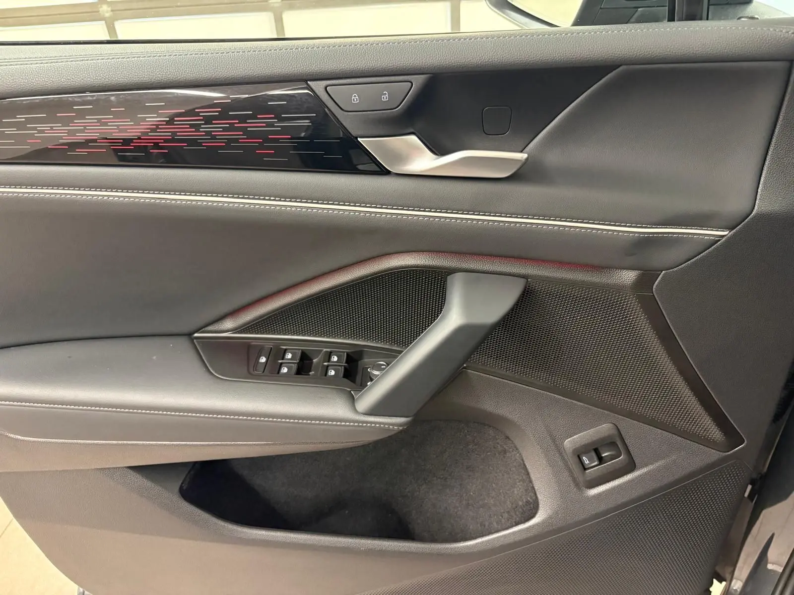 Vue intérieure côté gauche de la porte avant du Volkswagen Tiguan 2025, garniture noire avec surpiqûres blanches et bande décorative lumineuse.