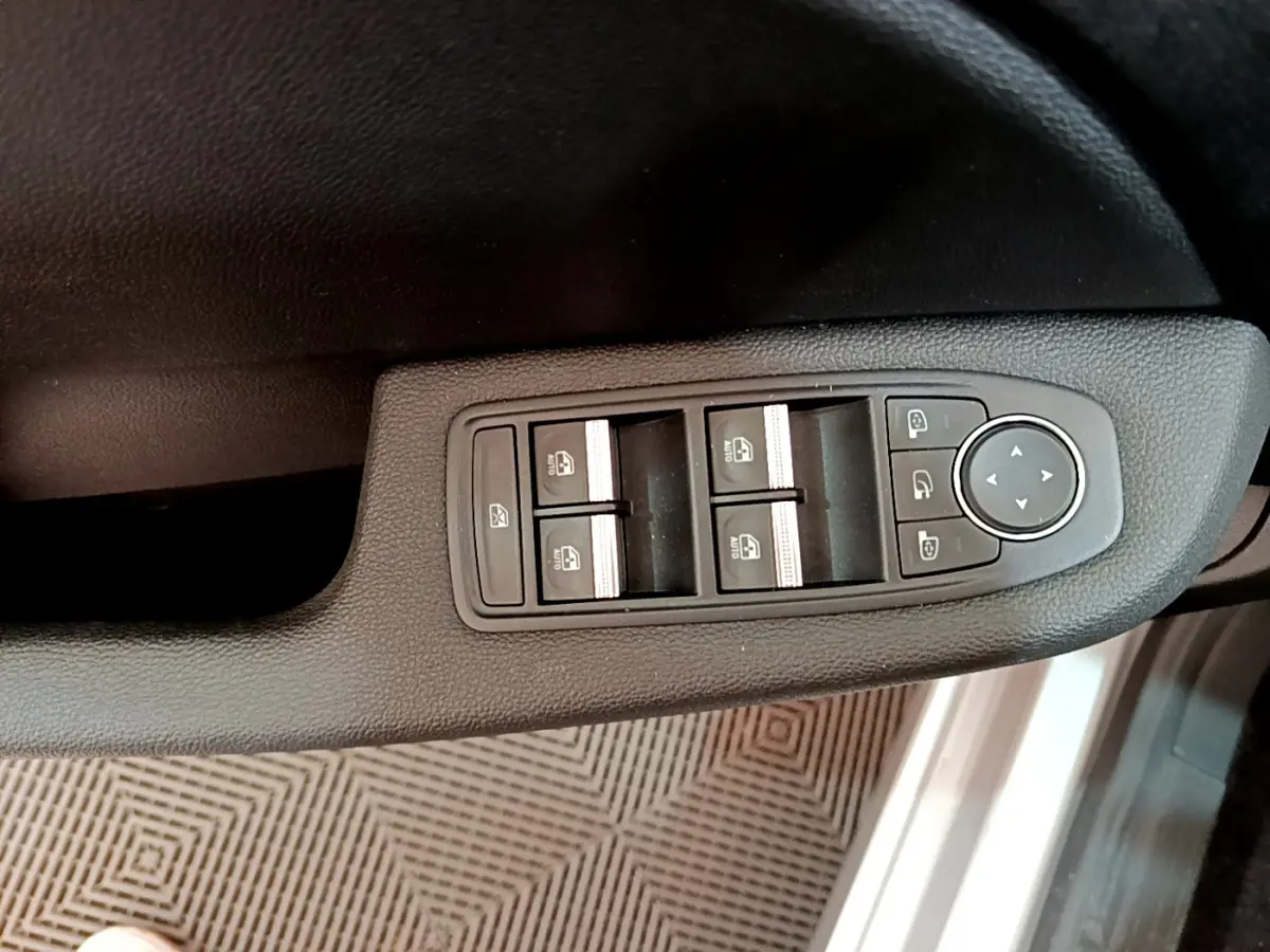 Vue rapprochée des commandes de lève-vitres et rétroviseurs sur la porte côté conducteur d’une Renault Clio gris clair.