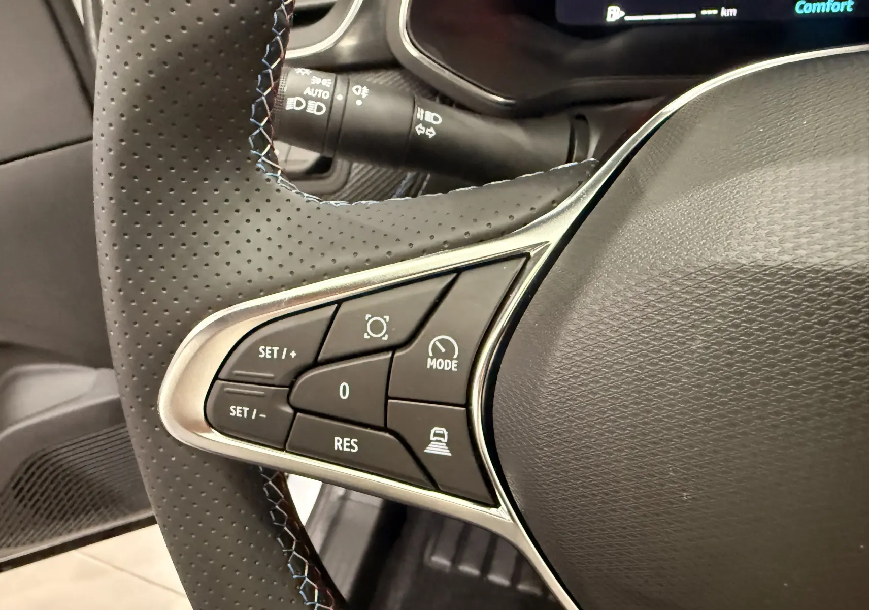 Gros plan sur les commandes gauche du volant perforé du Renault Captur blanc nacré, avec surpiqûres bleues et affichage numérique partiel.