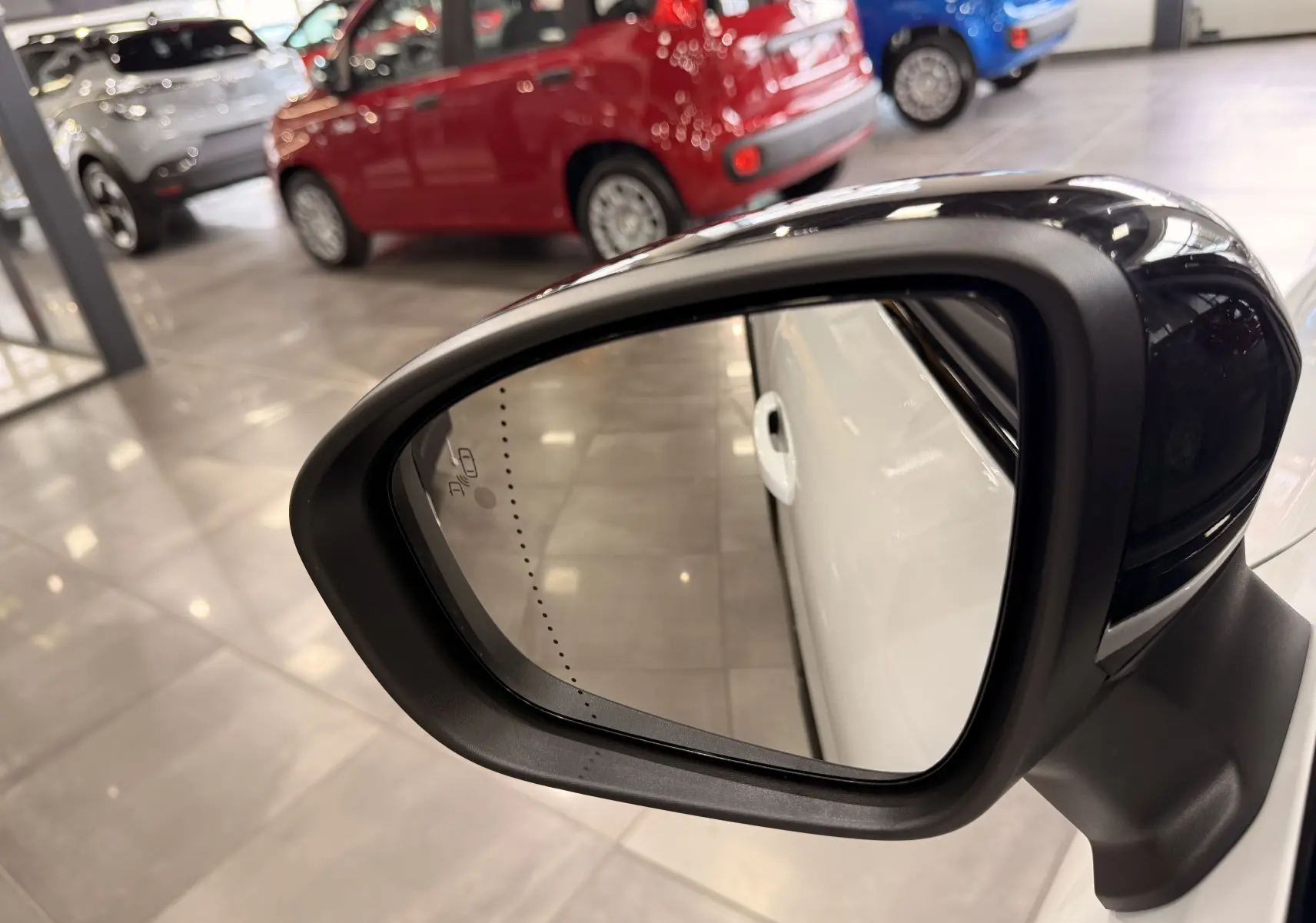 Rétroviseur côté droit noir brillant d’un Renault Captur blanc nacré avec toit noir, vue rapprochée en intérieur showroom.