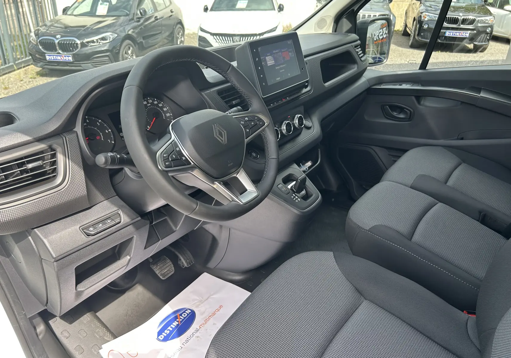 Vue intérieure côté conducteur du Renault Trafic Fourgon 2025, volant multifonction et écran tactile central visibles.