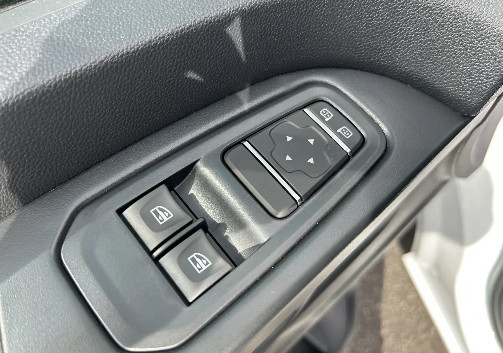 Gros plan sur les commandes de lève-vitres et réglage des rétroviseurs côté conducteur du Renault Trafic blanc.