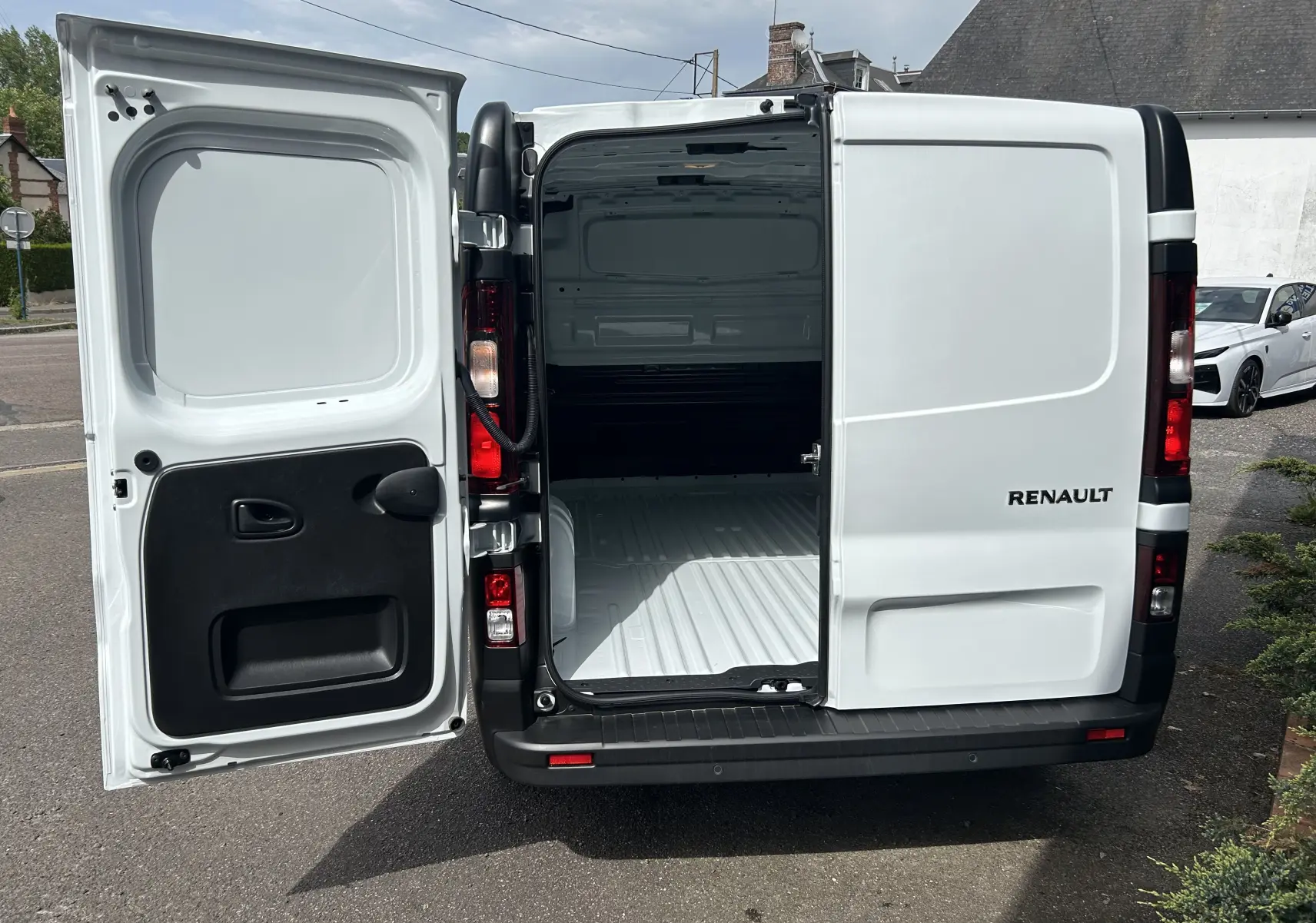 Vue arrière du Renault Trafic Fourgon blanc Glacier avec portes battantes ouvertes montrant l’espace de chargement vide.