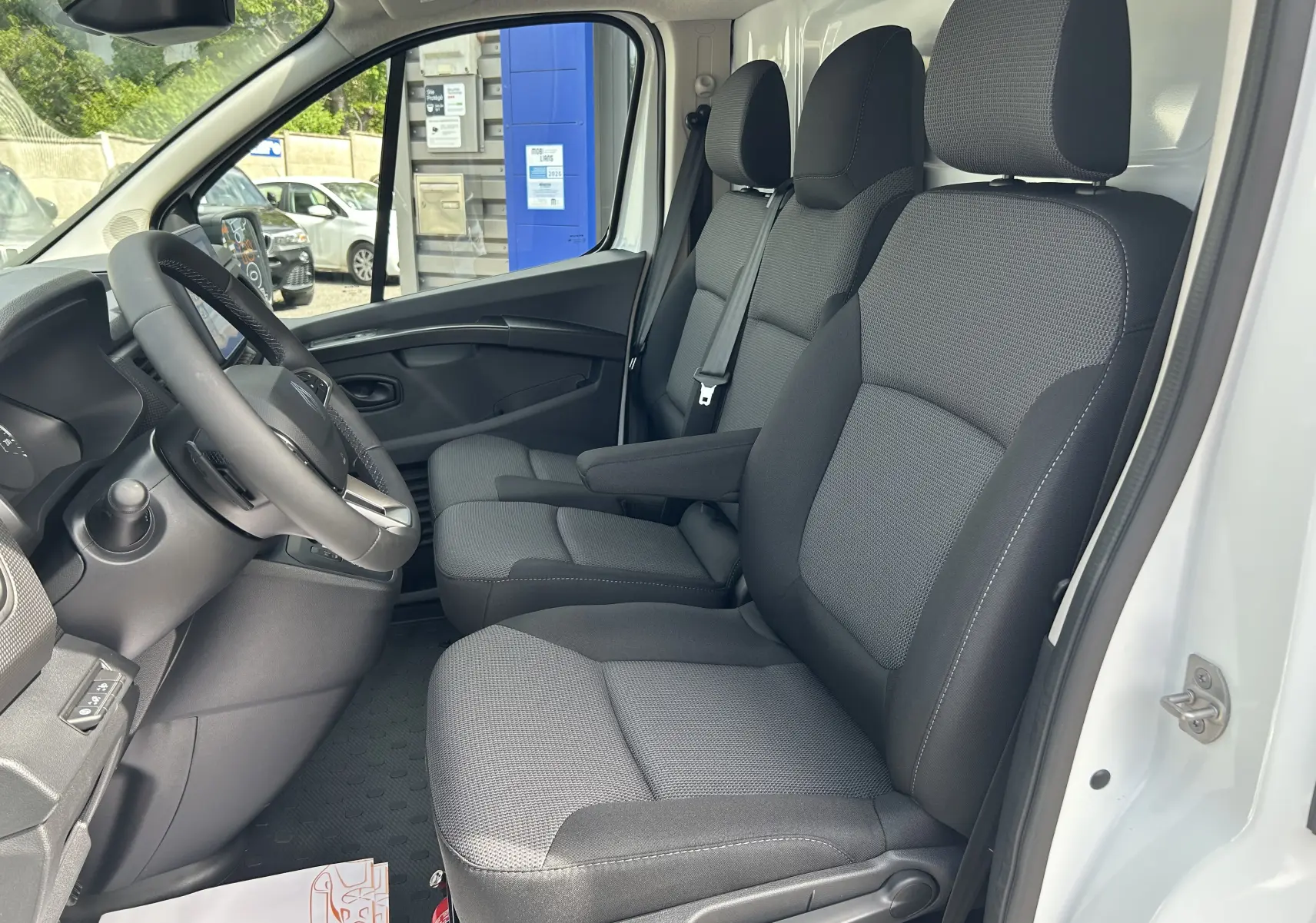 Vue intérieure côté conducteur du Renault Trafic Fourgon blanc glacier 2025, montrant les sièges tissu et le volant multifonction.