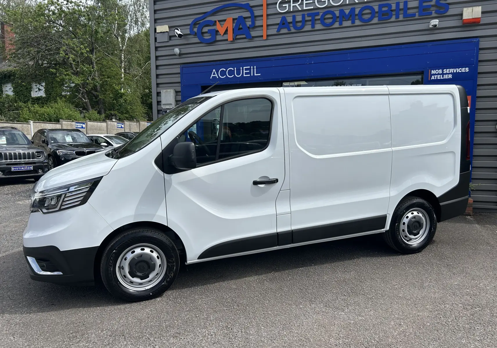 Vue de profil côté gauche d'un Renault Trafic Fourgon blanc Glacier stationné devant un garage automobile.