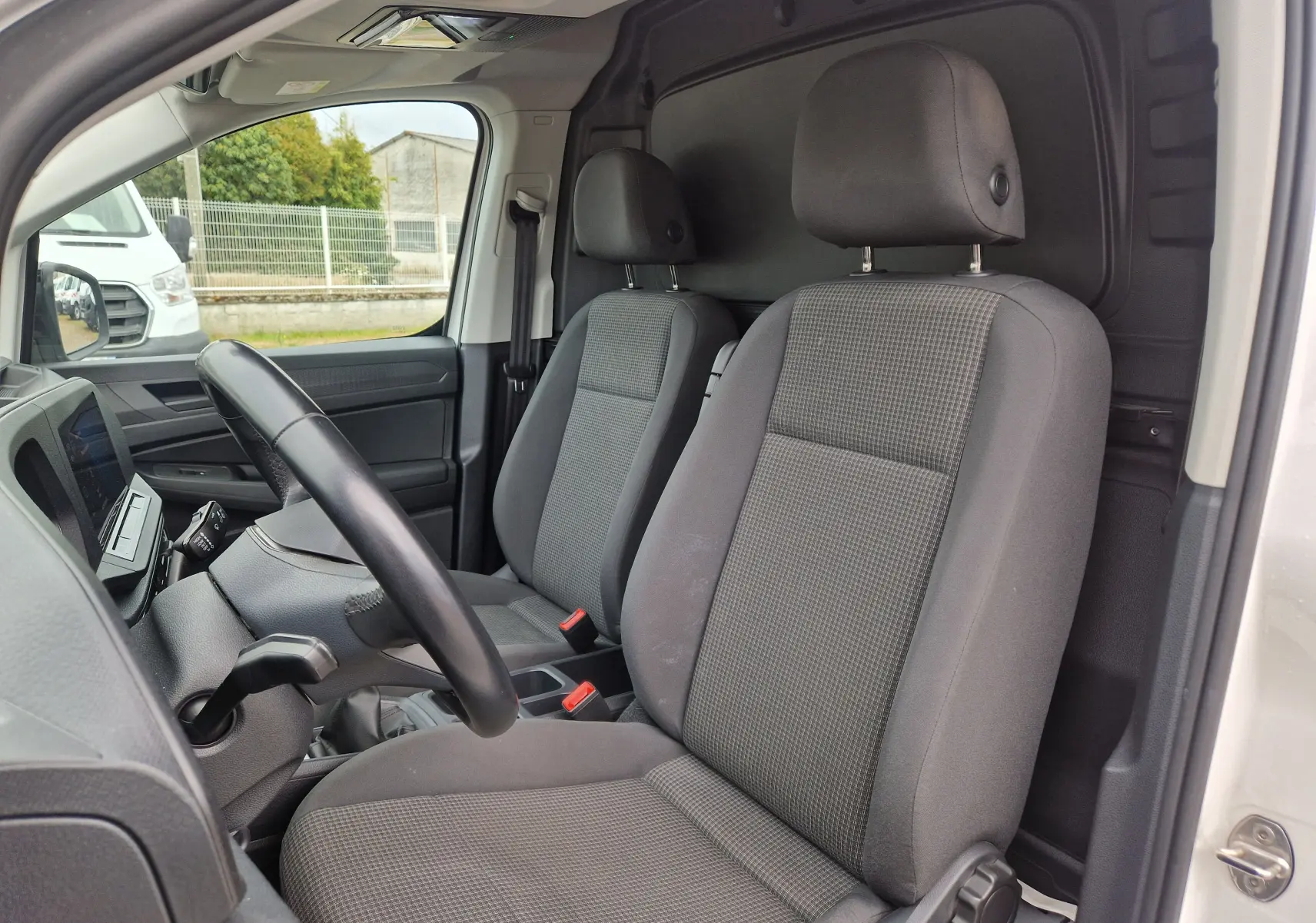 Vue intérieure côté conducteur du Volkswagen Caddy Cargo 2023, montrant les sièges gris et le tableau de bord.