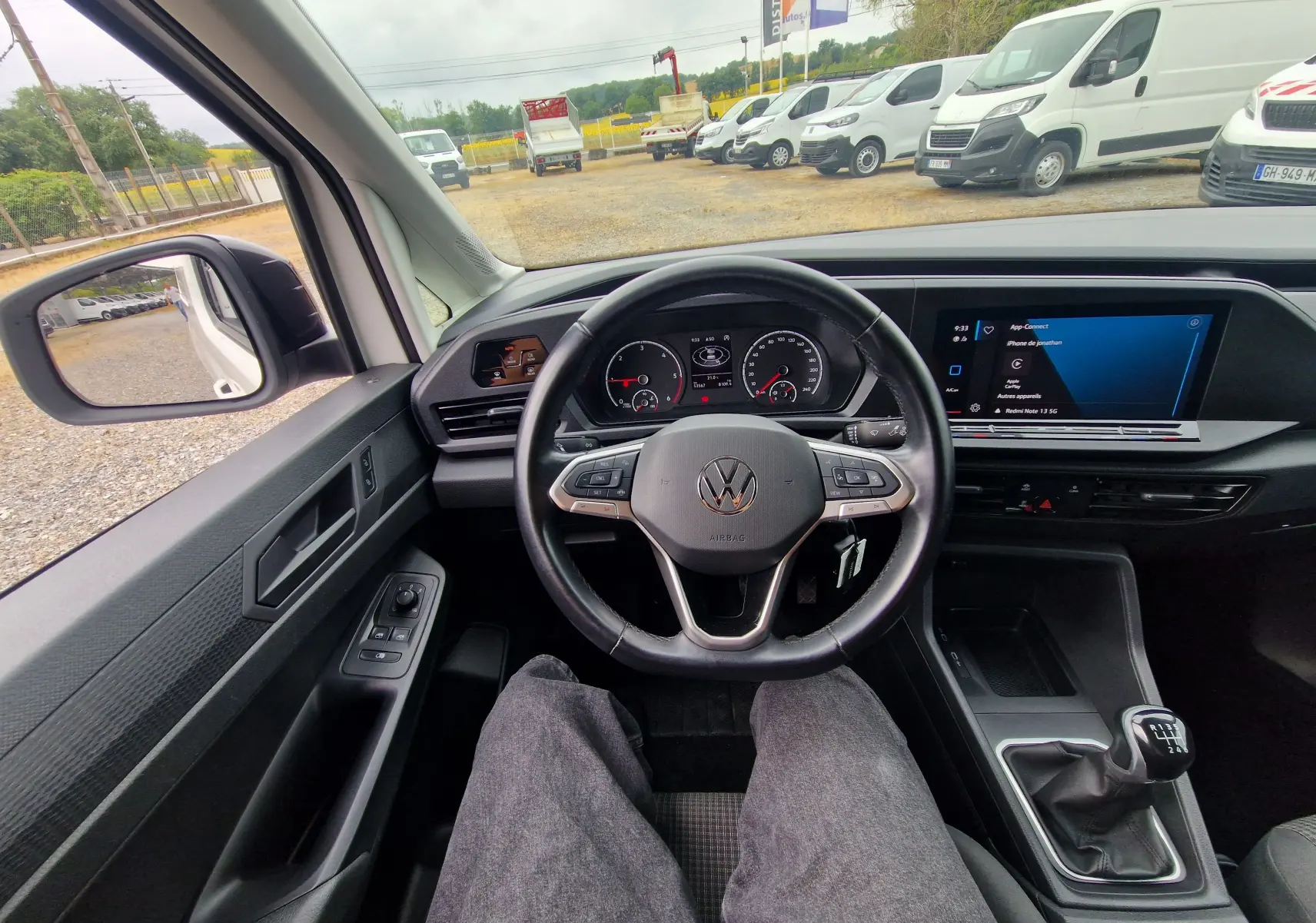 Vue intérieure depuis le siège conducteur du Volkswagen Caddy Cargo blanc 2023, volant multifonctions et boîte manuelle visibles.