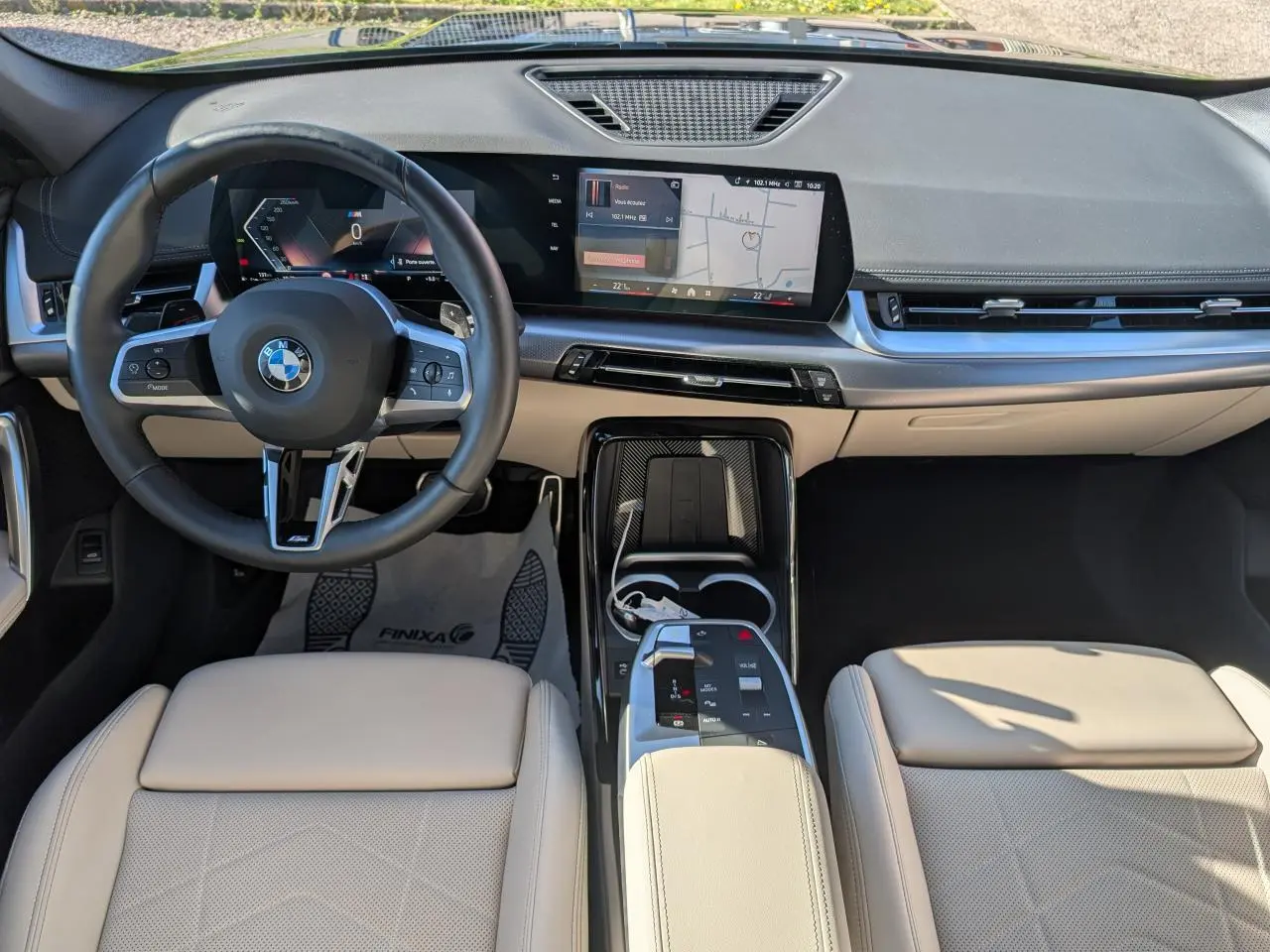Vue intérieure frontale du BMW X1 2024 M Sport avec sellerie similicuir Oyster claire et écran tactile incurvé.