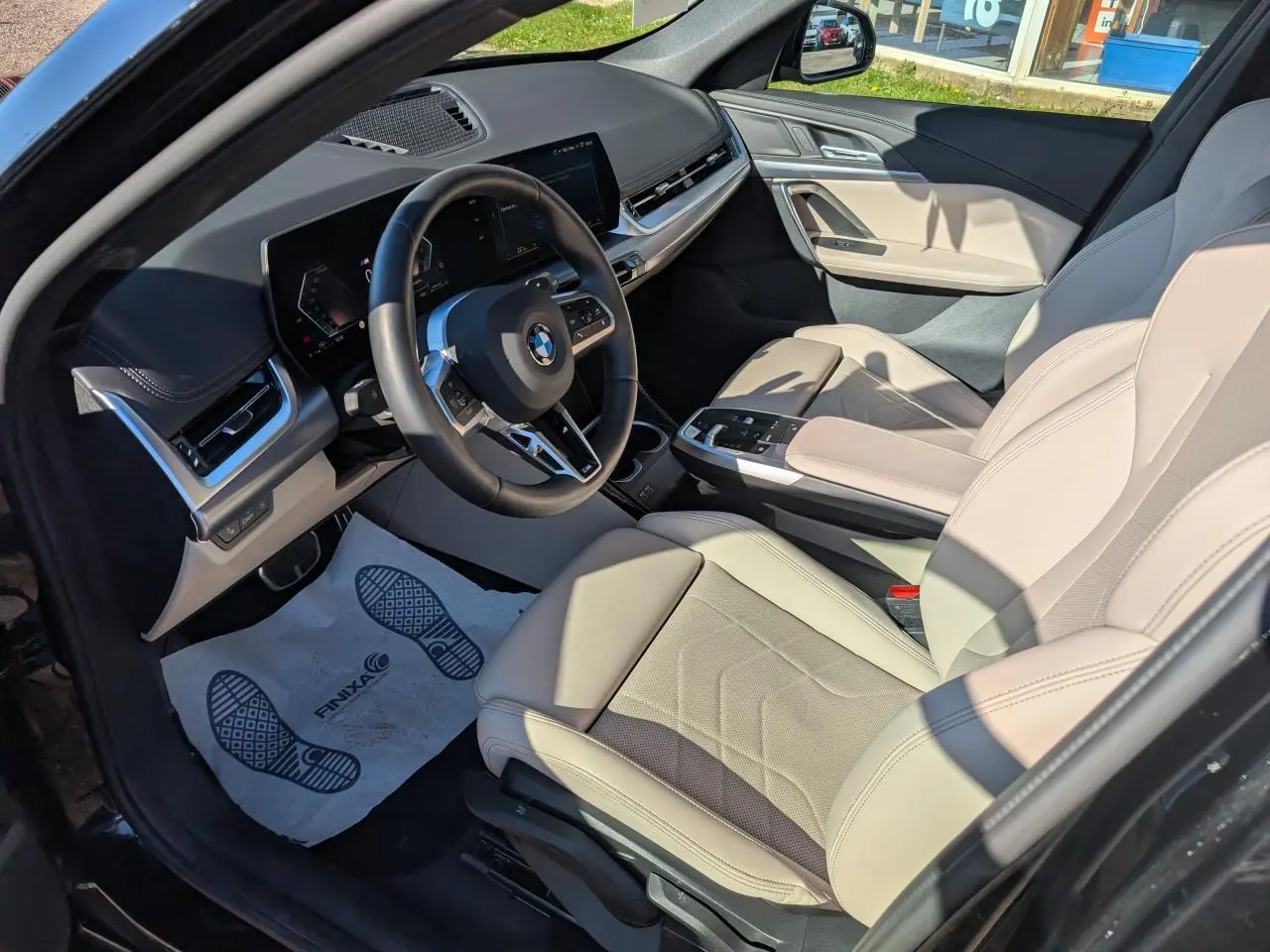 Vue intérieure côté conducteur du BMW X1 noir 2024, sellerie similicuir Oyster claire et tableau de bord moderne.