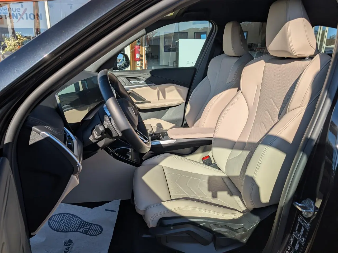Intérieur côté conducteur BMW X1 noir 2024, sièges sport similicuir Oyster beige et volant M cuir.