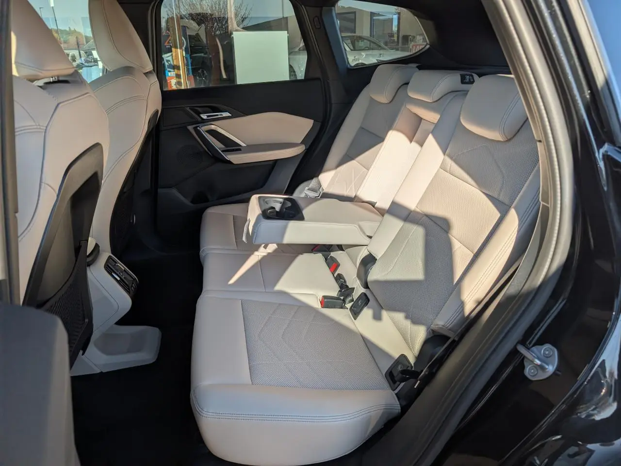 Vue intérieure côté droit sur la banquette arrière en similicuir Oyster du BMW X1 noir avec accoudoir central déployé.