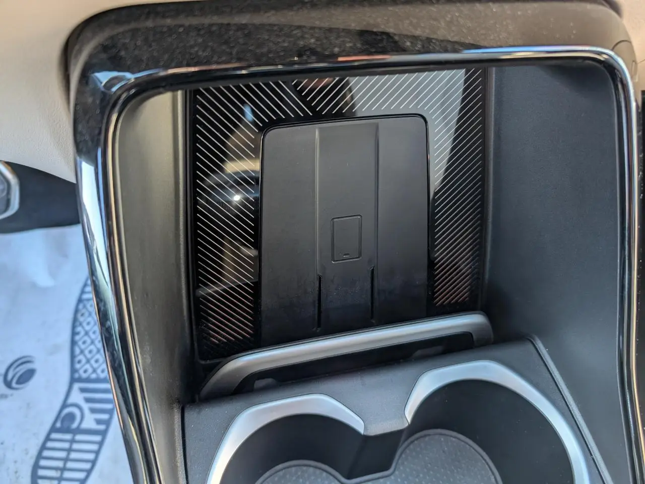 Détail de la console centrale noire du BMW X1 2024 avec zone de recharge sans fil et porte-gobelets intégrés.