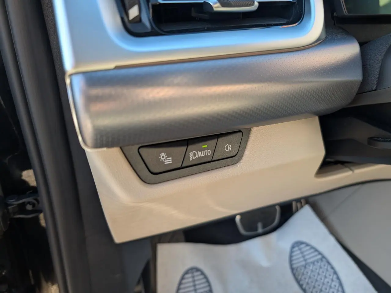 Détail intérieur côté gauche avec commandes d'éclairage sur tableau de bord beige et noir du BMW X1 noir 2024 M Sport.