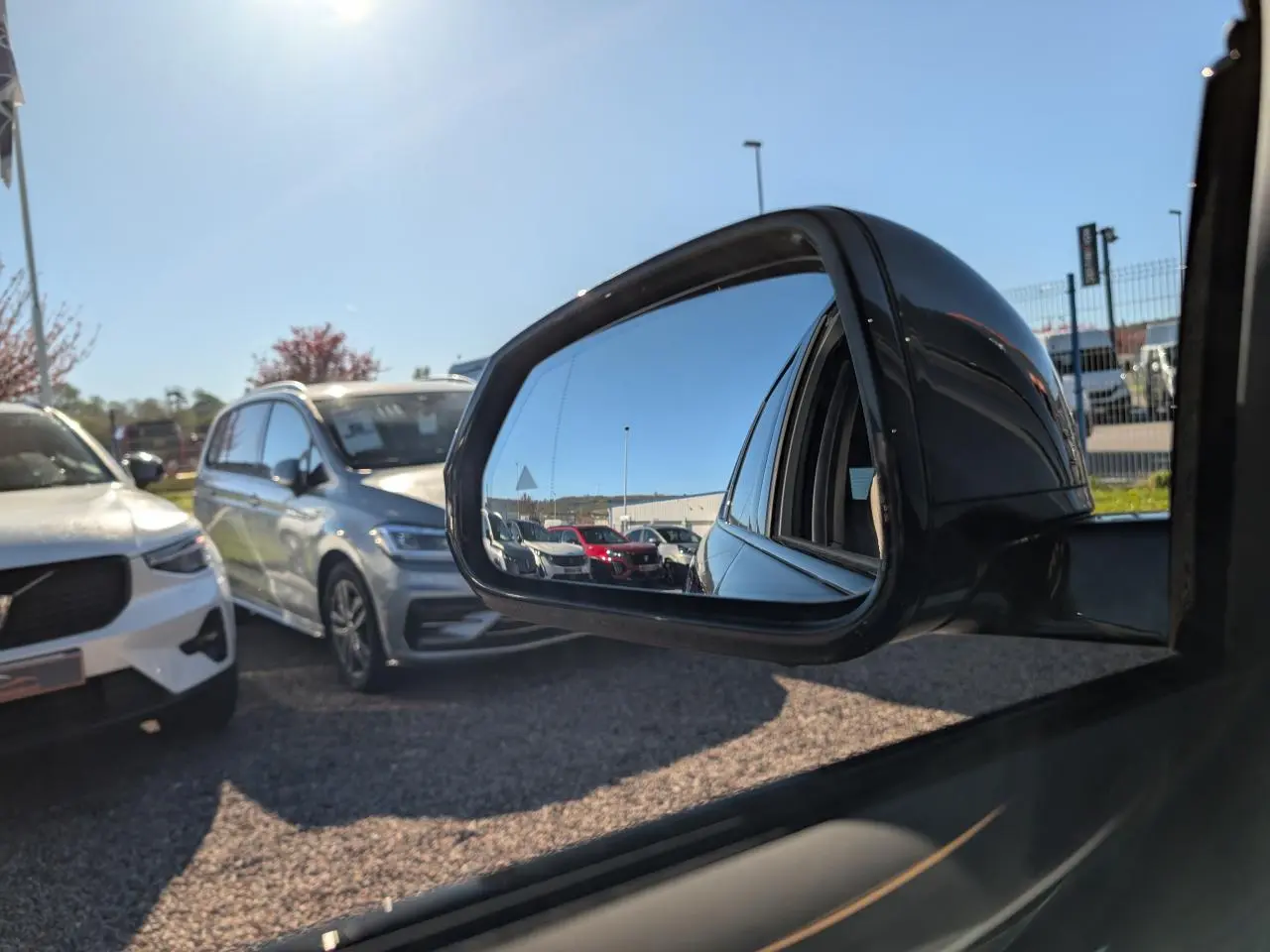 Rétroviseur extérieur droit noir du BMW X1 2024, reflétant plusieurs voitures sur un parking en plein jour.