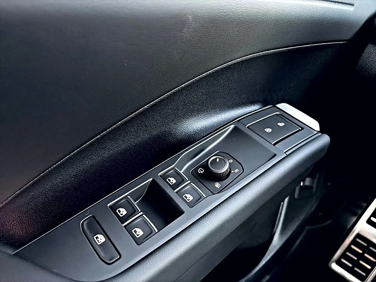 Gros plan sur la commande des vitres et rétroviseurs côté conducteur intérieur noir du Volkswagen T-Roc bleu céleste 2026.