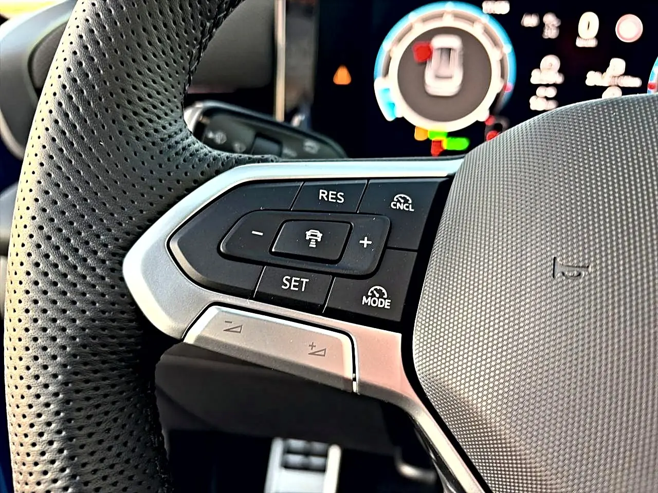 Gros plan sur les commandes multifonctions noires et argent du volant sport perforé du Volkswagen T-Roc bleu céleste 2026.