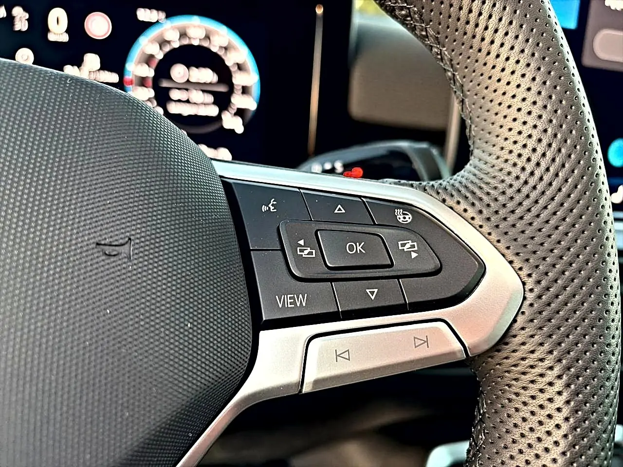 Gros plan sur le volant cuir perforé du Volkswagen T-Roc 2026 avec commandes multifonctions et affichage digital flou.