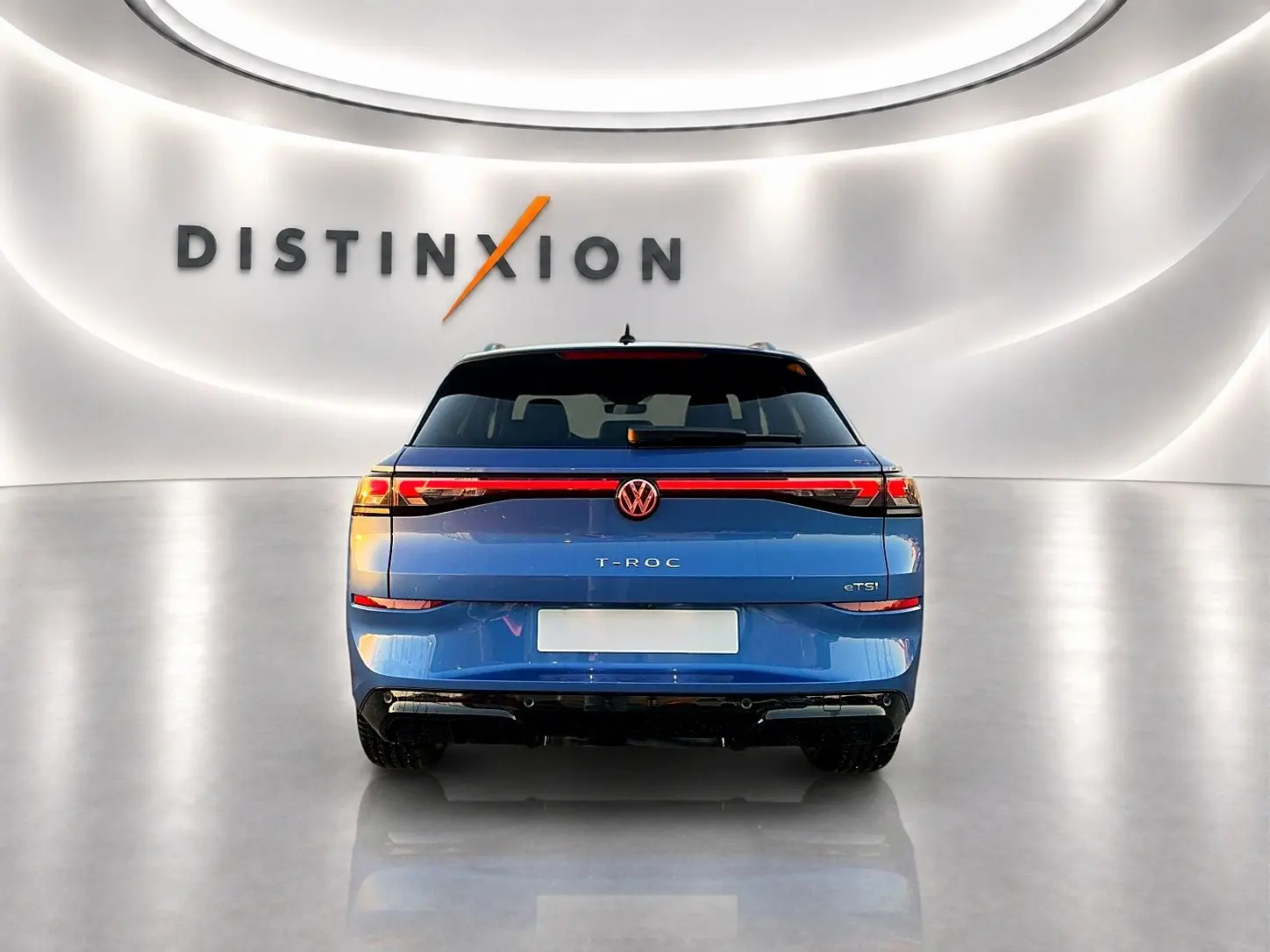 Vue arrière d'un Volkswagen T-Roc bleu céleste 2026 avec feux LED reliés et logo central lumineux.