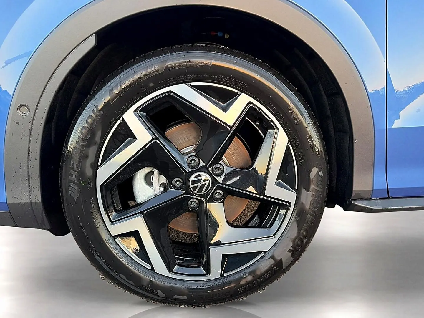 Gros plan sur la roue avant gauche d’un Volkswagen T-Roc bleu céleste avec jante alu noire et argentée au design géométrique.