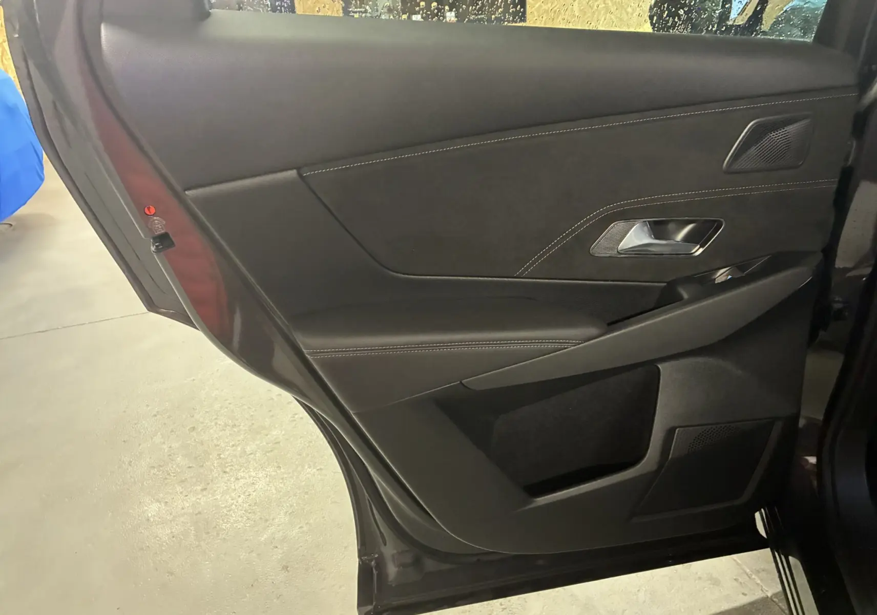 Vue intérieure de la porte arrière gauche du DS7 E-TENSE 2024 en gris, avec garniture noire et surpiqûres contrastées.