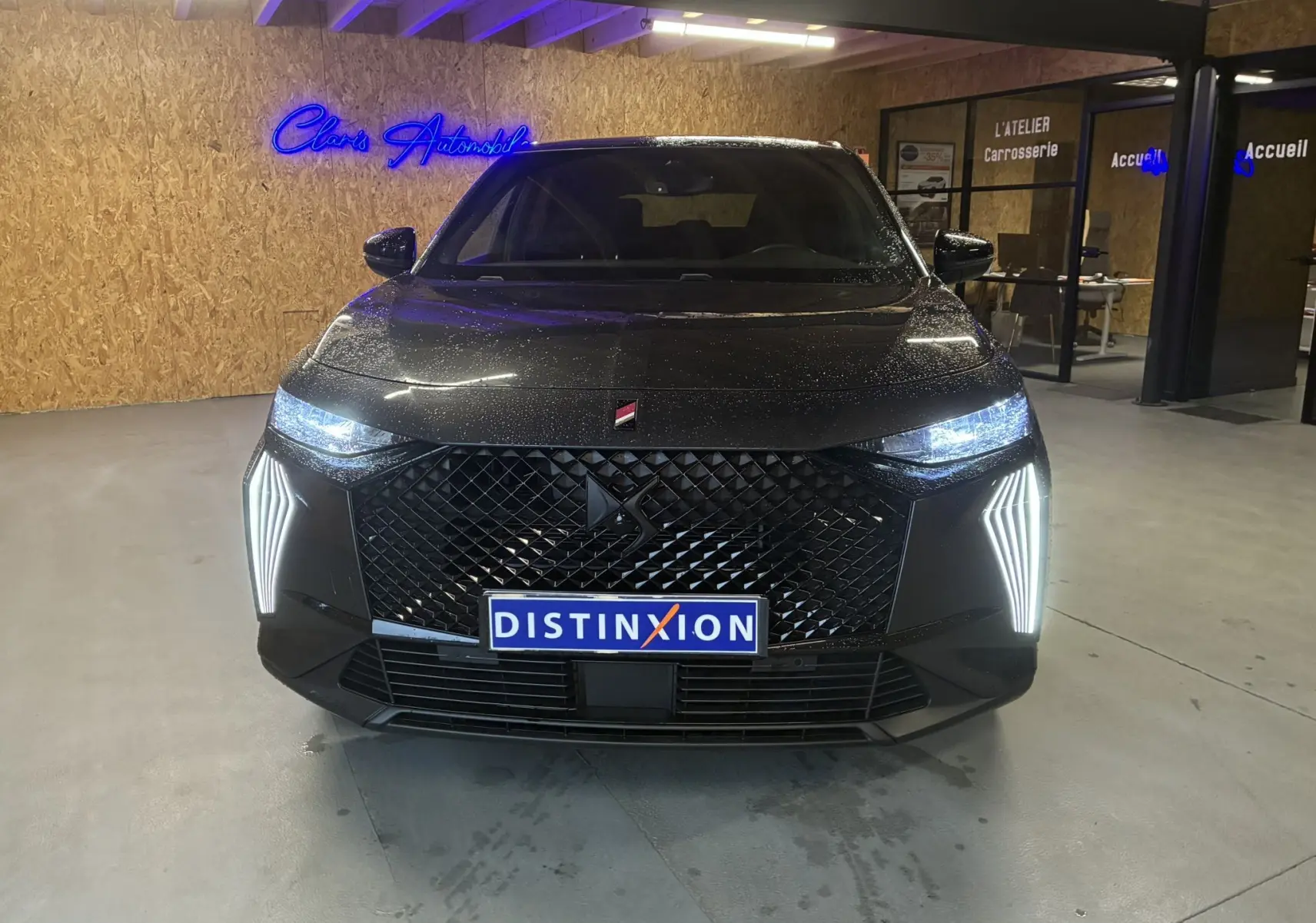 Vue avant d'un DS7 E-TENSE gris 2024 avec feux LED allumés et calandre noire en intérieur showroom.