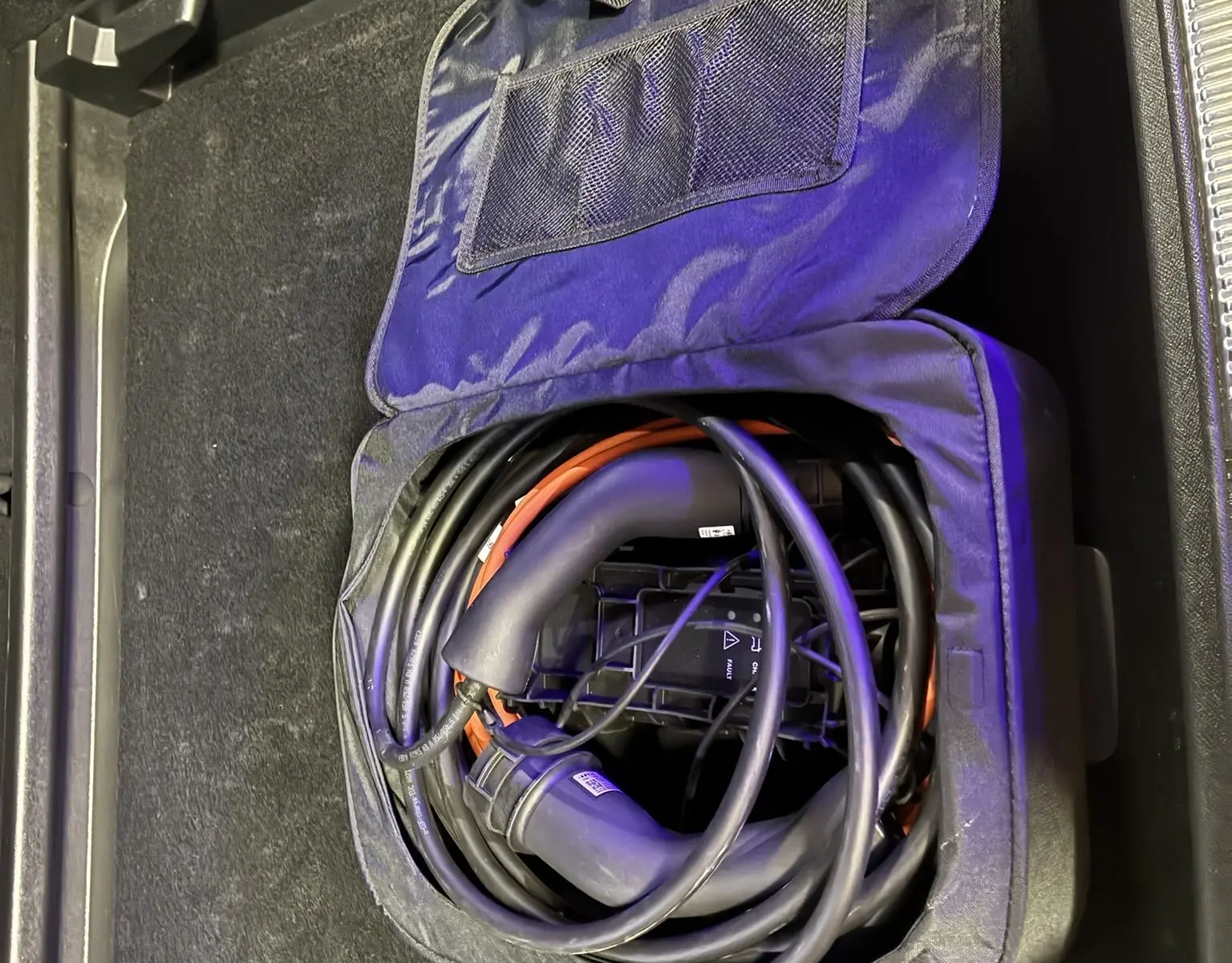 Câble de recharge hybride enroulé dans un sac noir, rangé dans le coffre d'un DS7 gris 2024.